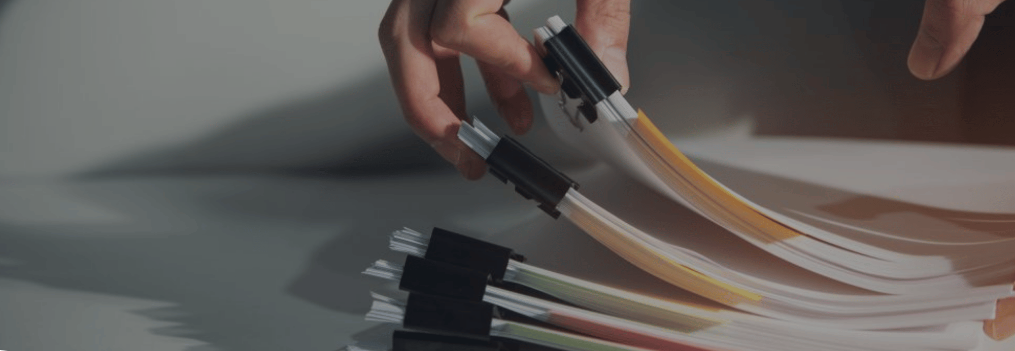 A close-up of hands handling a bundle of fiber optic cables with black connector sleeves and gold-colored internal strands, set against a dark gray background.