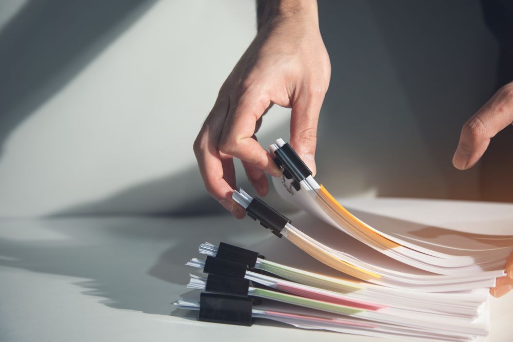 A close-up of hands handling a bundle of white document folders with black clips and colorful tabs on a light gray surface.